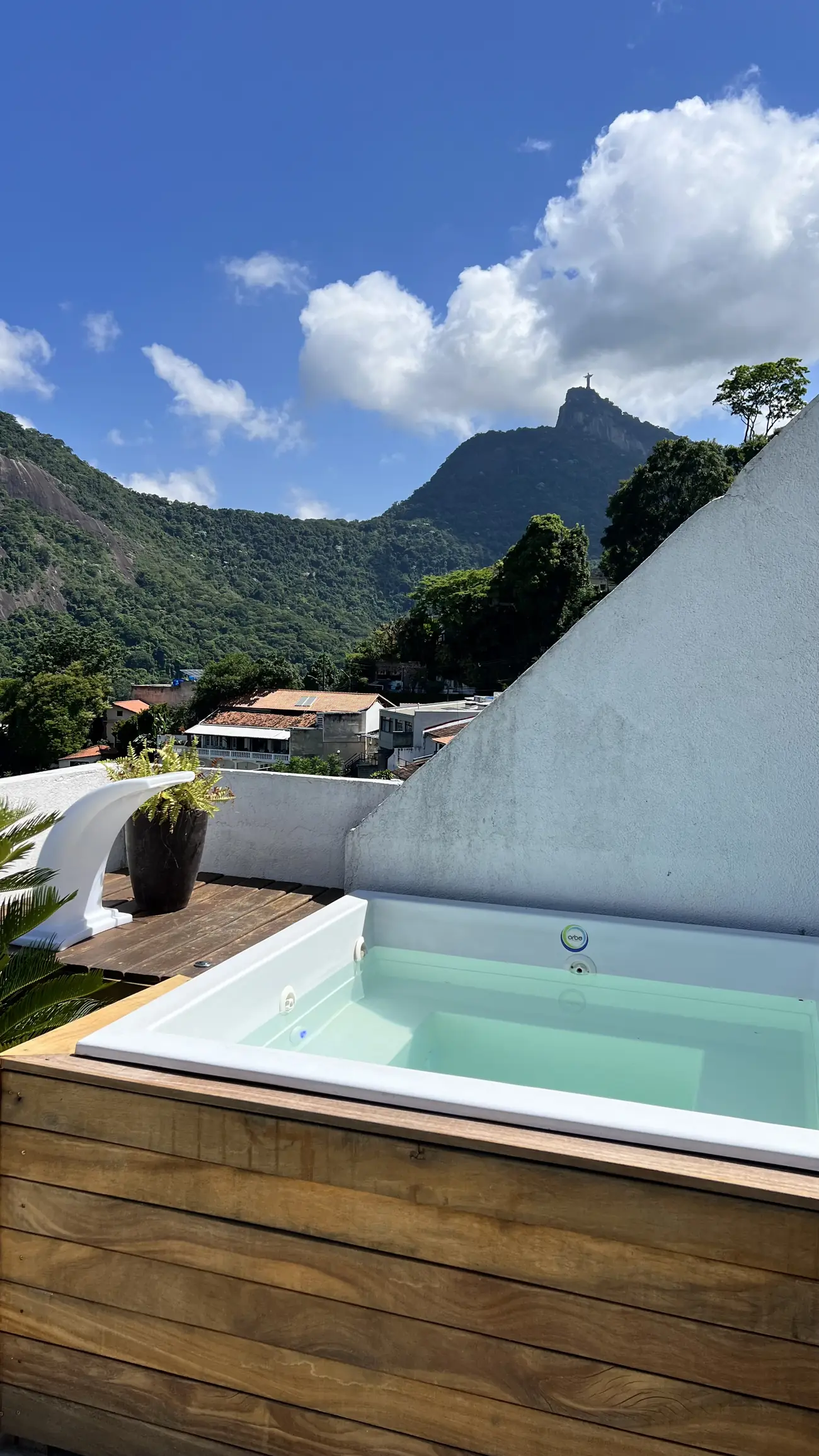 Ofurô em área externa com vista para o Cristo Redentor e montanhas ao fundo sob céu azul.